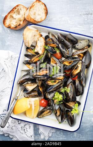 Barbecue tradizionale italiano Cozza blu con baguette e pomodori nel vino bianco come vista dall'alto su un vassoio Foto Stock