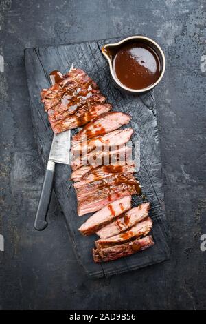 Tradizionale barbecue americano secco fianco invecchiato steak affettata con peperoncino Salsa come vista dall'alto su una vecchia scheda carbonizzato Foto Stock