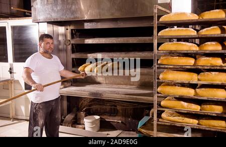 Lavoratore da forno tenendo fuori pane freschi Foto Stock