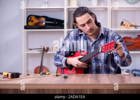 Giovane bello repairman riparazione di chitarra Foto Stock
