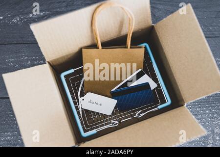 Ordini online conceptual still-life, Shopping basket all'interno di aprire il pacco di consegna con il prezzo di vendita dei tag e carte di pagamento Foto Stock