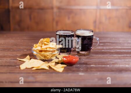 Due boccali di birra con spuntini sul tavolo di legno Foto Stock