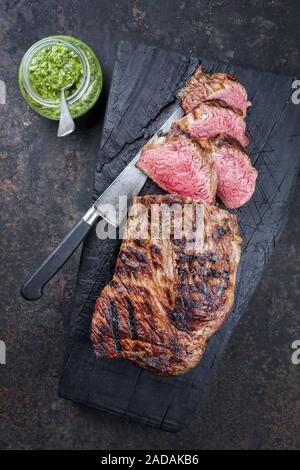 Barbecue argentino invecchiato secco wagyu tri Punta di manzo con salsa chimichurri come dip come vista dall'alto su un carbonizzato scheda di legno Foto Stock