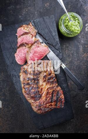 Barbecue argentino invecchiato secco wagyu tri Punta di manzo con salsa chimichurri come dip come vista dall'alto su un carbonizzato scheda di legno Foto Stock