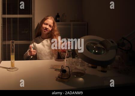 Felice ragazza seduta al tavolo in laboratorio e mostrando il pollice verso l'alto. il concetto di hobby e istruzione Foto Stock