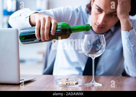 Dipendente di sesso maschile di bere alcolici e fumare sigarette a workpla Foto Stock