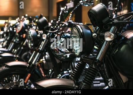 Close up dettaglio dei fari anteriori e le parti cromate di motociclette, nuovissima moto parcheggiate in una fila in una concessionaria di moto. Profondità di campo Foto Stock