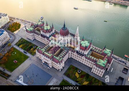 Budapest, Ungheria - Aerial drone vista del bellissimo Parlamento di Ungheria al tramonto con luci d'oro sul fiume Danubio, imbarcazioni turistiche e tradi Foto Stock