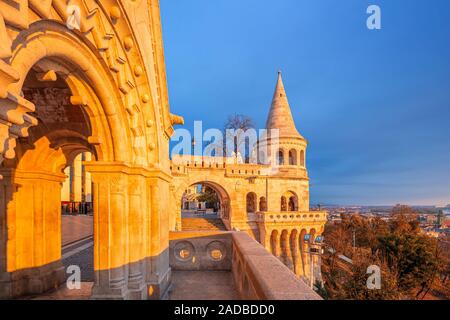 Budapest, Ungheria - famoso bastione dei pescatori in golden shine a sunrise presi da un balcone. Cielo blu chiaro, foglie di autunno e il fogliame in backgroun Foto Stock