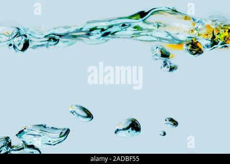 Vista laterale di un increspata superficie di acqua miscelata con olio vegetale e le bolle in isolati contro un fondo azzurro. Foto Stock