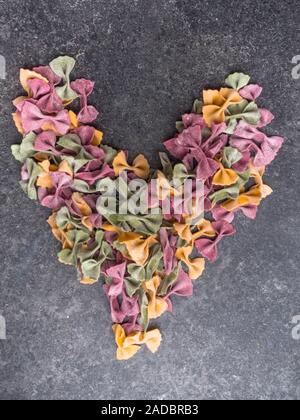 Colorata secca pasta italiana sulla superficie di marmo, forma di cuore fatta di farfalle o tagliatelle Foto Stock