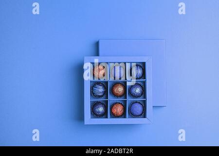 Cioccolatini fatti a mano in un riquadro blu su un neon di sfondo blu. Appartamento vista dall'alto. Copia dello spazio. Concetto di vacanza minimalismo. Telaio orizzontale Foto Stock