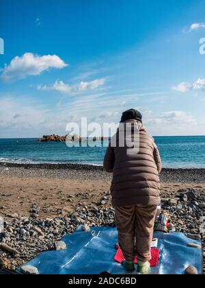 Donna Sciamano eseguendo shamanist rituale, ocean beach, vicino underwater tomba del re Munmu di Silla, segnato da rocce Daewangam, Gyeongju, Corea del Sud Foto Stock