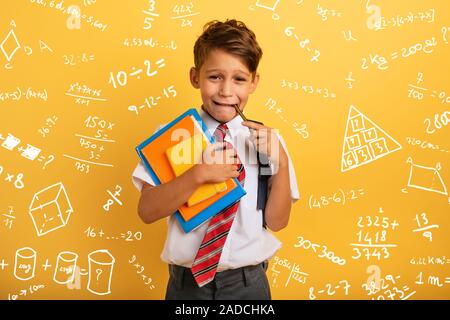 Bambino piange perché ha un sacco di compiti di scuola. Espressione emotiva. Sfondo giallo Foto Stock