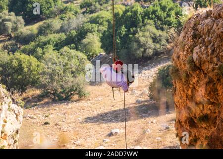 Turistico-scalatore incombe sull'abisso giù sotto di lui è una spessa, bella e verde sentiero forestale, nel nord di Israele Foto Stock