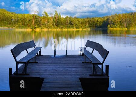 Dock o il molo sul lago nel giorno d'estate. Passerella vuota con due panche in Bielorussia Foto Stock