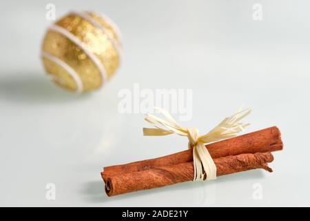 Luminose ancora in vita con una chiusura di bastoncini di cannella con un archetto su una bianca lastra di vetro e una golden natale Pallina in background Foto Stock