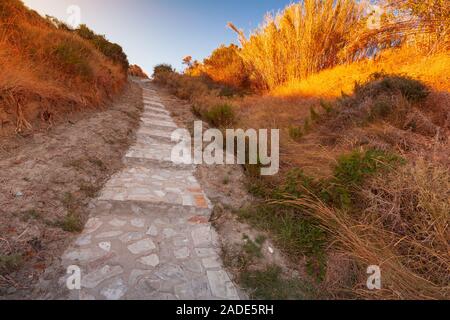 Rurale passerella in ciottoli prospettiva, scale in pietra andare fino in prossimità di erba costiere nella luce del sole di mattina Foto Stock