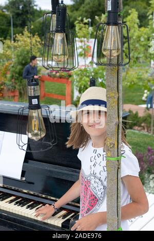 Giovane ragazza adolescente in posa di un cappello vicino al pianoforte su un giorno di estate nel parco Foto Stock