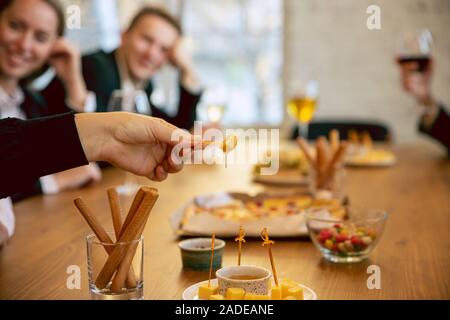 Felice co-lavoratori celebra durante la festa aziendale, per eventi aziendali. Giovani uomini caucasici in abbigliamento business parlare, bere vino e mangiare spuntini. Concetto di ufficio cultura, il lavoro di squadra, amicizia, weekend. Foto Stock