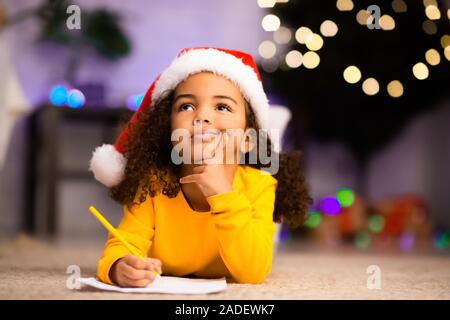 Malinconica poco ragazza afro pensando di lettera a Babbo Natale Foto Stock