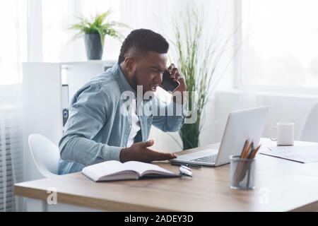 Imprenditore deluso parlando al telefono e guardando il laptop con rabbia Foto Stock