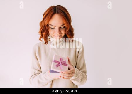 Ragazza giovane con Umore festive sorride dolcemente, tenendo in mano un pastello colorato di rosa confezione regalo con un nastro. Donna felice, spiata all'interno di una confezione regalo. Foto Stock