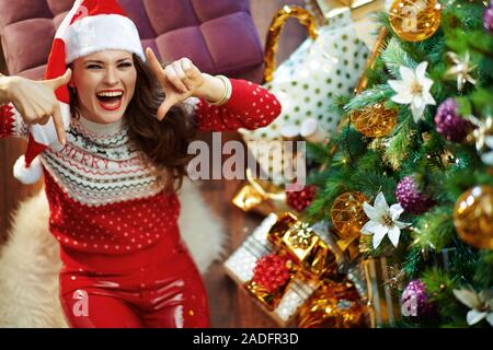 Vista superiore di sorridere alla moda di 40 anno vecchia donna con lunghi capelli bruna indossando rosso bianco Natale maglione e elf santa hat inquadratura con le mani sotto Foto Stock