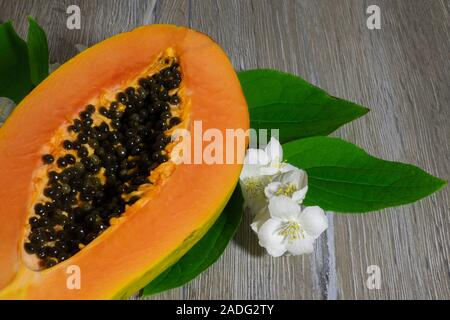 Fresco affettato papaia con semi all'interno su un sfondo di legno con fiori di gelsomino. La metà del giallo papaya Foto Stock