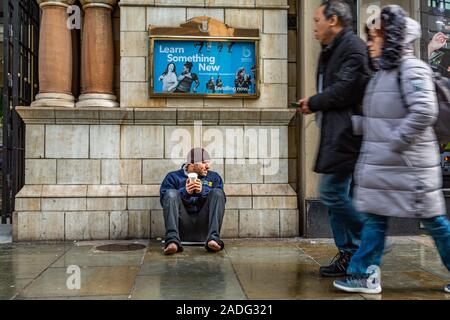 L'uomo senza scarpe seduto a mendicare per denaro in inverno, come persone corsa passano senza prendersi cura, vicino alla stazione di Liverpool Street Londra Inghilterra REGNO UNITO Foto Stock