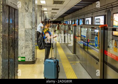 Una donna che guarda un telefono attende il treno alla stazione di Chongwenmen Interchange sulla linea 2 e sulla linea 5 della metropolitana di Pechino, Pechino Cina Foto Stock