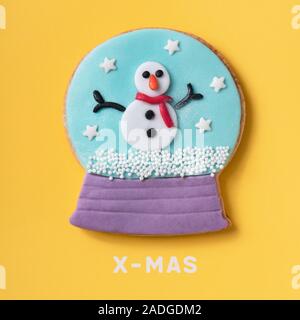 Un cookie in forma di Snow Globe, con un pupazzo di neve all'interno e il testo x-mas su sfondo giallo Foto Stock