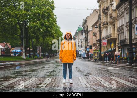 La donna in mezzo alla strada strada di attraversamento in impermeabile giallo Foto Stock