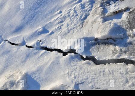 Spaccatura nel ghiaccio su un lago ghiacciato o fiume in inverno. Sfondo di neve, di consistenza Foto Stock