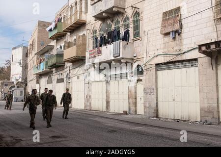 Hebron, West Bank. 4 dicembre, 2019. IDF soldati pattugliare una 'ghost Street', una volta vivace con il commercio ma chiusa ai palestinesi dopo il 1994 i disordini. Difesa israeliano Ministro Bennett ha recentemente annunciato la sua approvazione della costituzione di un nuovo quartiere ebraico nella prevalentemente città palestinese di Hebron nei pressi del vecchio mercato di frutta e verdura. I terreni acquistati dagli ebrei che vi risiedono nei primi anni del XIX secolo, fu abbandonato dopo il 1929 massacro in cui 67 ebrei furono assassinati dai rivoltosi arabi. Credito: Nir Alon/Alamy Live News. Foto Stock