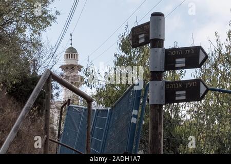 Hebron, West Bank. 4 dicembre, 2019. Un minareto della moschea è raffigurato nei pressi di segni in ebraico dirigere ai quartieri ebraici a Hebron. Difesa israeliano Ministro Bennett ha recentemente annunciato la sua approvazione della costituzione di un nuovo quartiere ebraico nella prevalentemente città palestinese di Hebron nei pressi del vecchio mercato di frutta e verdura. I terreni acquistati dagli ebrei che vi risiedono nei primi anni del XIX secolo, fu abbandonato dopo il 1929 massacro in cui 67 ebrei furono assassinati dai rivoltosi arabi. Credito: Nir Alon/Alamy Live News. Foto Stock