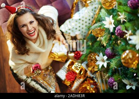 Vista superiore della felice elegante medioevo donna con lunghi capelli bruna in oro zecchino gonna e maglione bianco sotto albero di Natale decorato nei pressi di presen Foto Stock