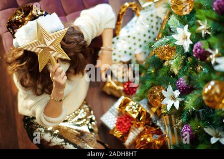 Vista superiore della mezza età della donna con lunghi capelli bruna in oro zecchino gonna e maglione bianco sotto albero di Natale decorato nei pressi di caselle presenti holdin Foto Stock