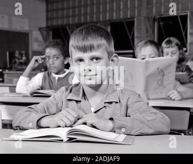 Anni sessanta CAUCASIAN ragazzo seduto alla scrivania in Aula cercando in telecamera African American Girl dietro guardando lui - s15731 HAR001 HARS capretti elementari del viso diverse informazioni di comunicazione differenti lieta gioia lifestyle femmine spazio copia amicizia espressioni maschi B&W contatto visivo di grado scuole felicità testa e spalle allegro afro-americani afro-americano nero di conoscenza dell'etnia a integrato principale collegamento sorride gioiosa vari VARIO GRADO DI COOPERAZIONE SCUOLA LUI NOVELLAME BIANCO E NERO ETNIA CAUCASICA HAR001 in vecchio stile afro-americani Foto Stock