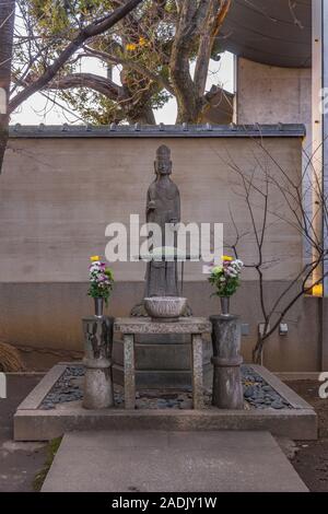 Statua di pietra raffigurante il Buddha Yakushi Nyorai con due vasi riempiti con i crisantemi in Tokyo Tennoji. Foto Stock