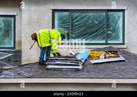 Concetto di processo di costruzione. Esperto onstruction worer aggiungendo un asfalto ghiaia tetto su una casa nuova, lavorando sotto la pioggia. Foto Stock