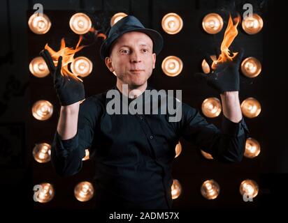 Professional illusionista in black hat, camicia e glowes giocando con il fuoco Foto Stock