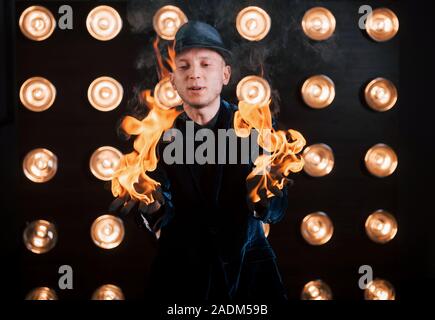 Il fuoco è nelle sue mani. Professional mago mostra trick. Lampadine della luce sullo sfondo Foto Stock