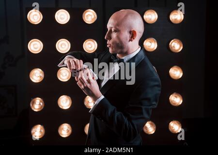 A concentrarsi a difficile muoversi. Mago in abito nero e con carte da gioco in piedi in camera con illuminazione speciale al backstage Foto Stock