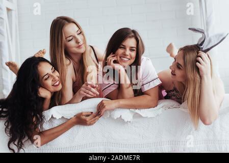 Avendo una conversazione amichevole. Gioiosa le ragazze in calzature sdraiato sul letto in camera bianca e hanno la celebrazione Foto Stock