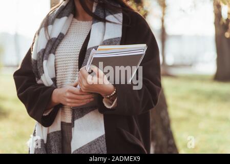 Foto ritagliata. Giovani brunette sorge nel parco vicino agli alberi e mantiene il blocco note Foto Stock