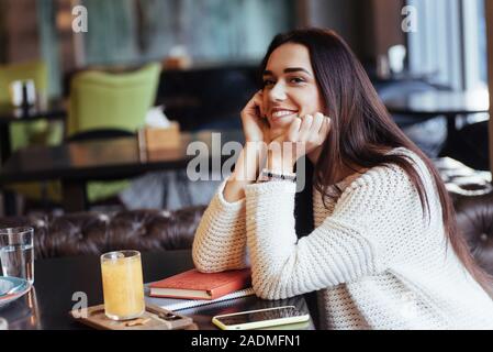 Bella donna. Allegro ragazza bionda sedersi nel ristorante con bevanda gialla sul tavolo e sorrisi Foto Stock