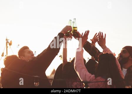 Bottiglie fino. Vacanze sul tetto. Allegro gruppo di amici ha sollevato le mani con alcool Foto Stock