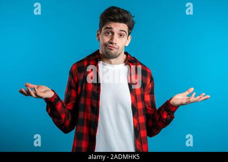 Giovane bello sicuri guy in rosso plaid shirt alza le spalle le sue braccia, Fa gesto di non so, non aiutano a nulla. Foto Stock