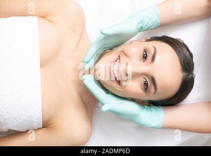 Le mani nei guanti di gomma con attenzione toccando il volto di donna sorridente Foto Stock